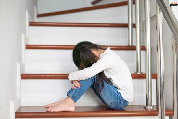an upset child with her head and hands on her knees sitting in the stair