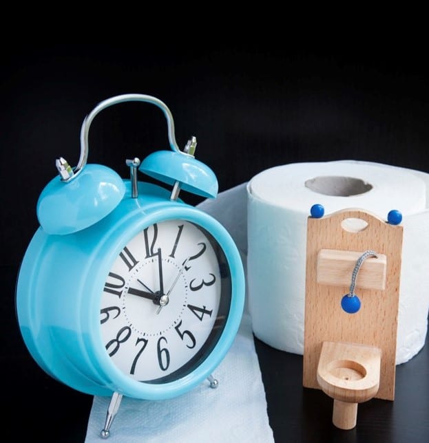 Wooden toy toilet, toilet paper and alarm clock on black background