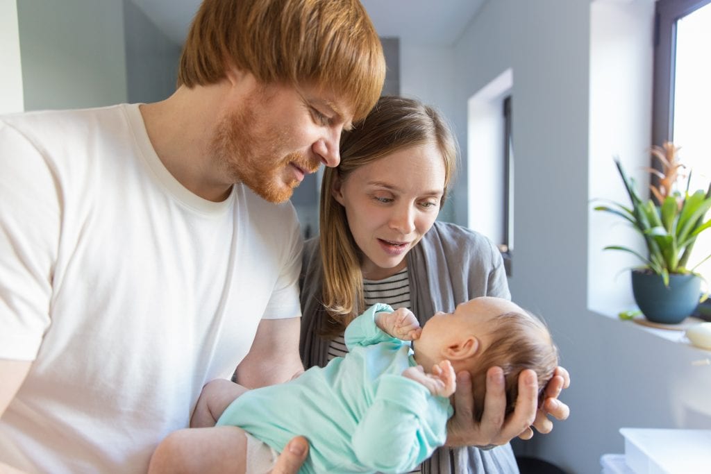 New mother and father holding and cuddling baby in arms. Family portrait of couple and cute little child in home interior. Happy parenthood concept