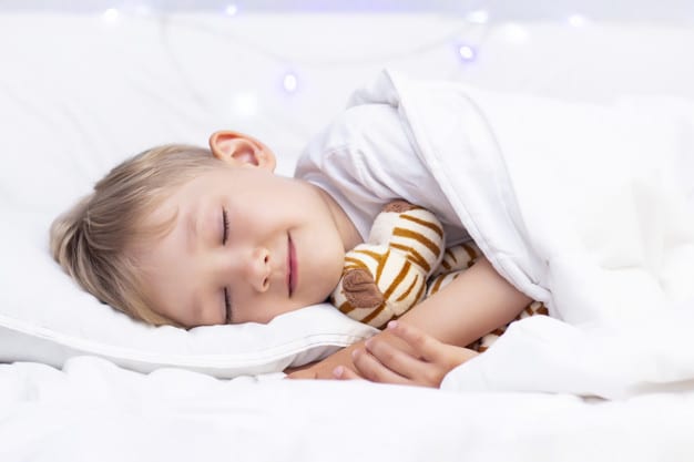 Charming little white boy sleeps in bed. hugs a soft toy