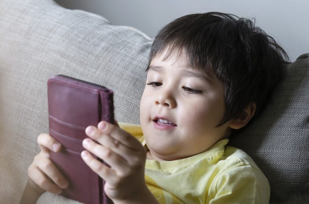 Close up Cute boy watching cartoons on mobile phone,Preschool kid with smiling face lying on sofaChild typing on cell phone while relaxing