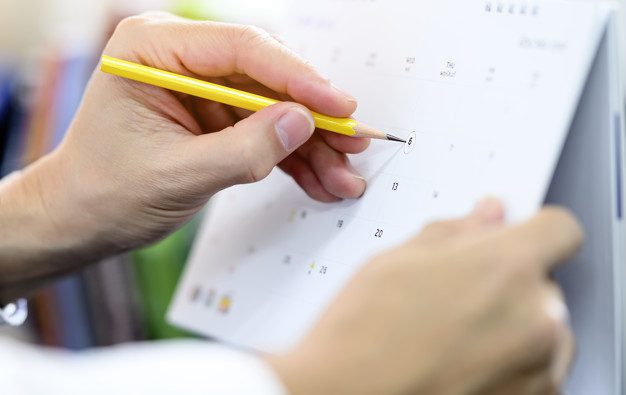 Cropped view of man hand holding yellow pencil circling the date on calendar.