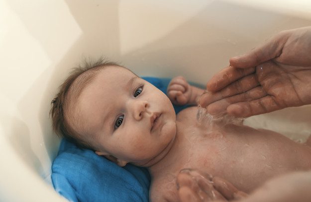 Hygiene and care for baby. Unrecognizable father bathing her son in white small plastic bat. Portrait of a baby is being bathed by his father using tub at home. Soft tone. Bath time for a cute little newborn baby