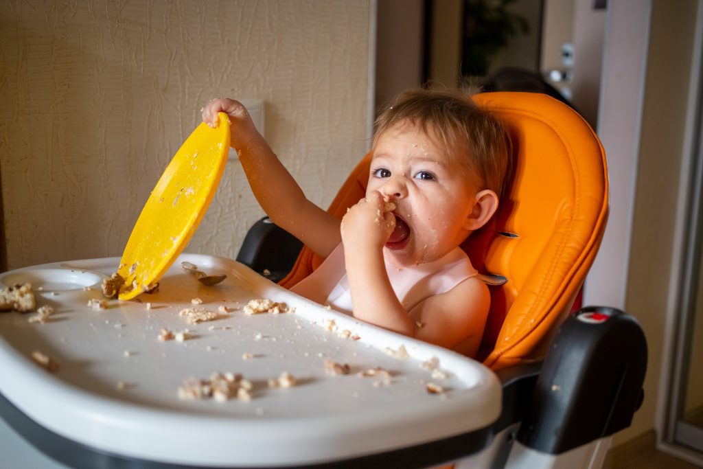 adorable baby plays with  plate at the table. little child indulges in a baby chair after eating