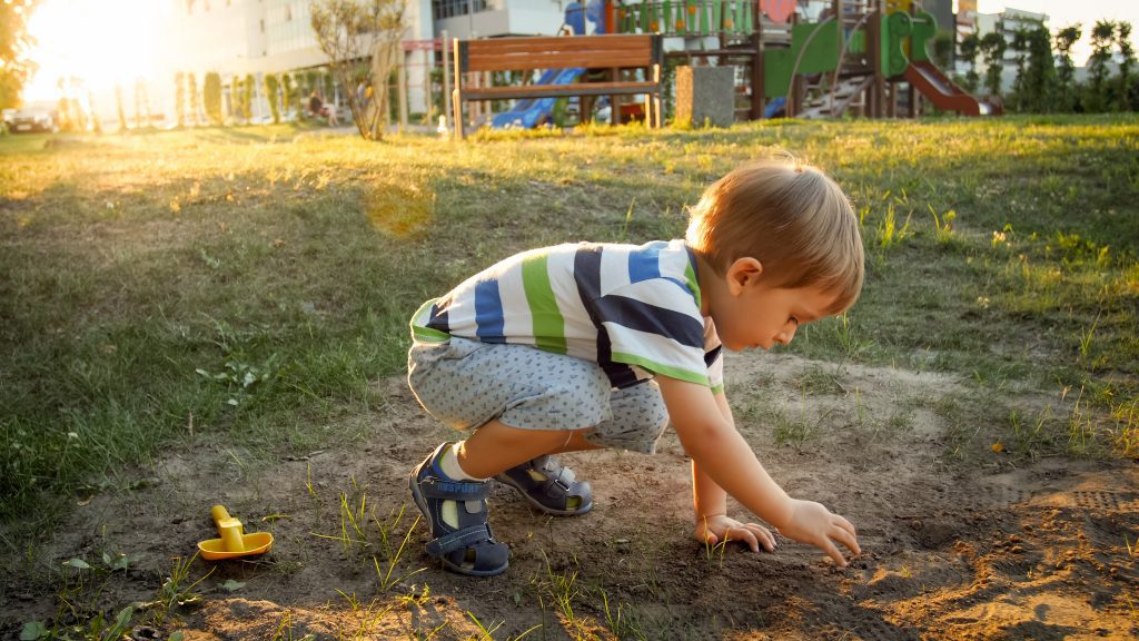 Image of 3 years old little boy sitting on the ground at park and digging sand