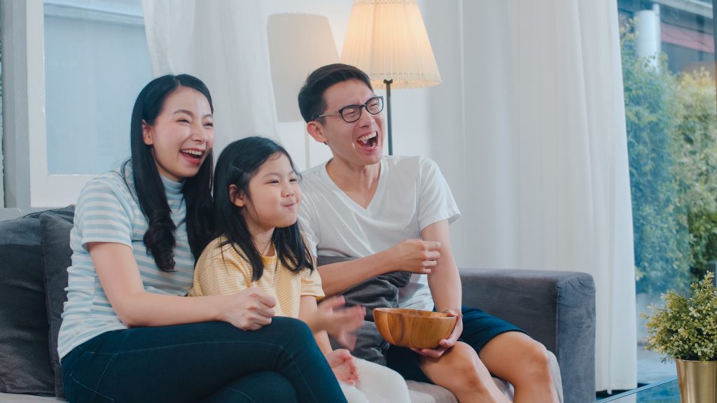 Asian family enjoy their free time relax together at home. Lifestyle dad, mom and daughter watch TV together in living room in modern home at night concept.