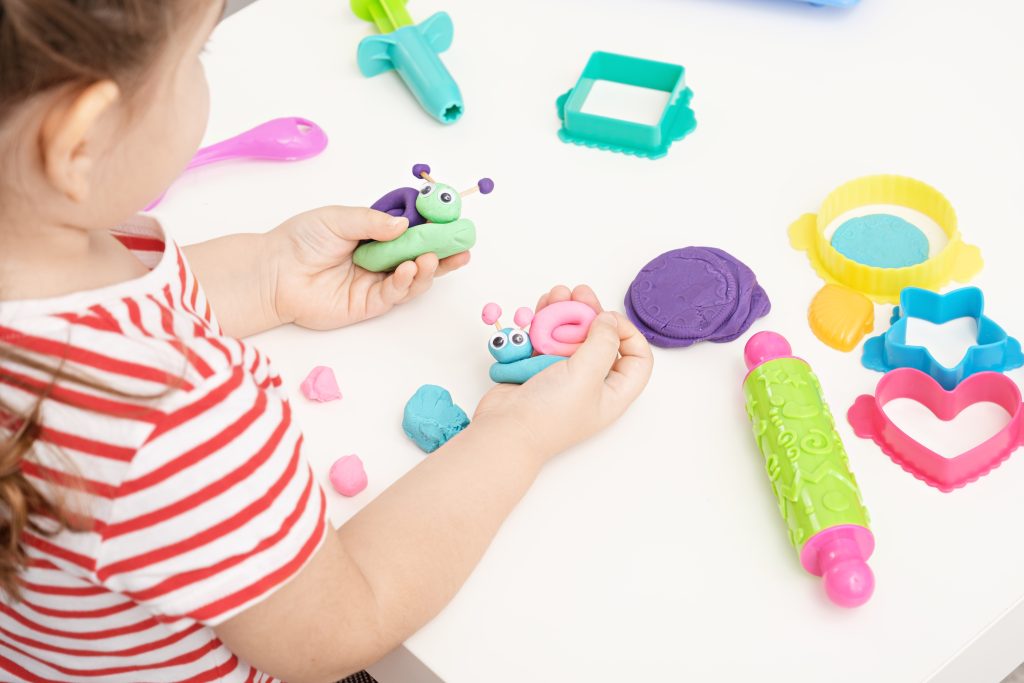 baby girl playing with plasticine on white table, sculpting figures snails, home educational games, colorful play dough concept