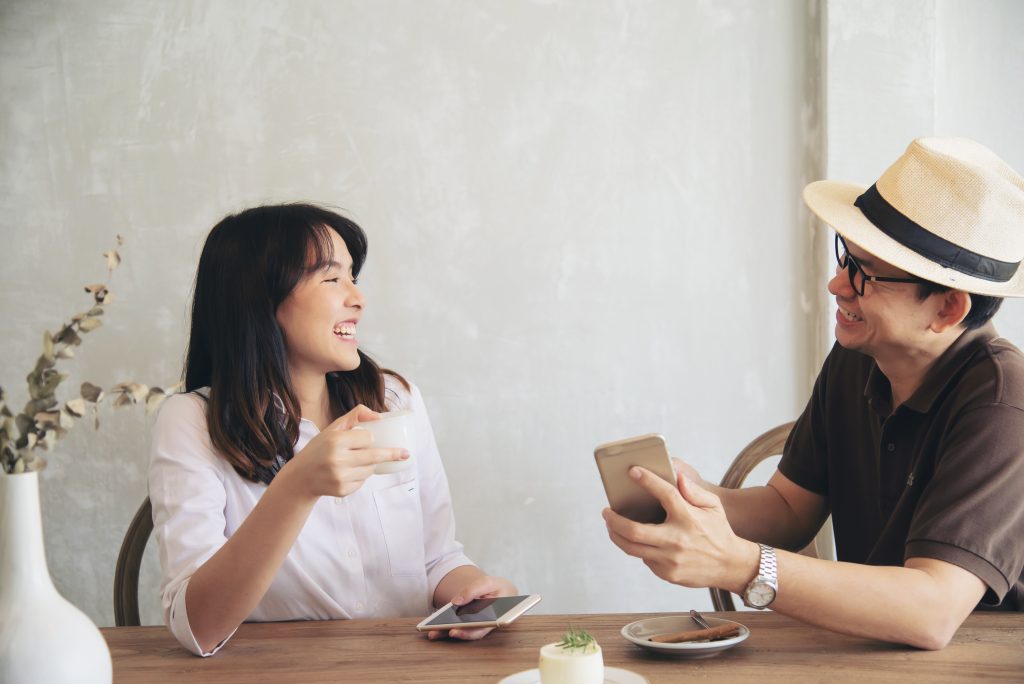 Casual man and woman talking happily while drink coffee and looking mobile phone - happy time lifestyle in coffee shop