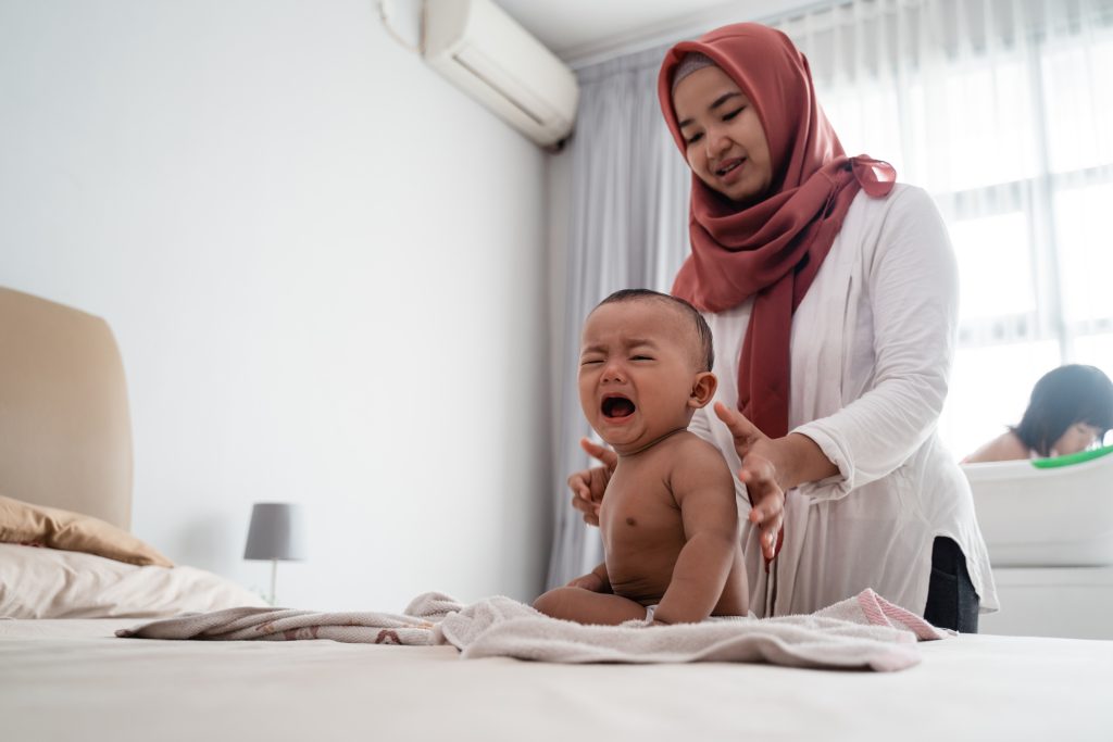 muslim mother applying baby oil to her baby boy after a bath